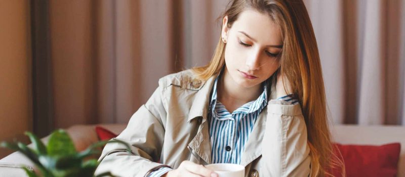 Unemployed woman sits alone heartbroken at coffee shop dwelling in sadness about her lack of career